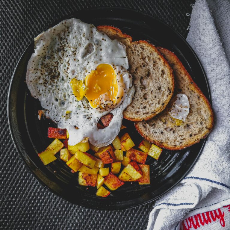 A mouthwatering breakfast of fried egg and toast with seasoned potatoes, beautifully presented.