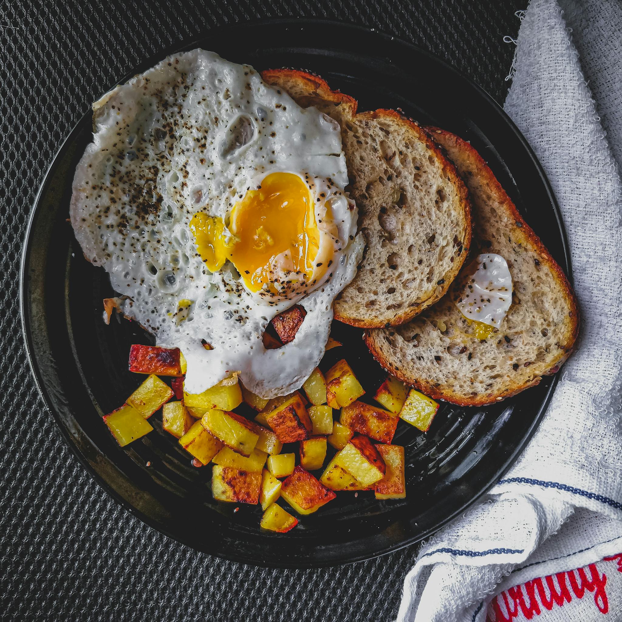 A mouthwatering breakfast of fried egg and toast with seasoned potatoes, beautifully presented.